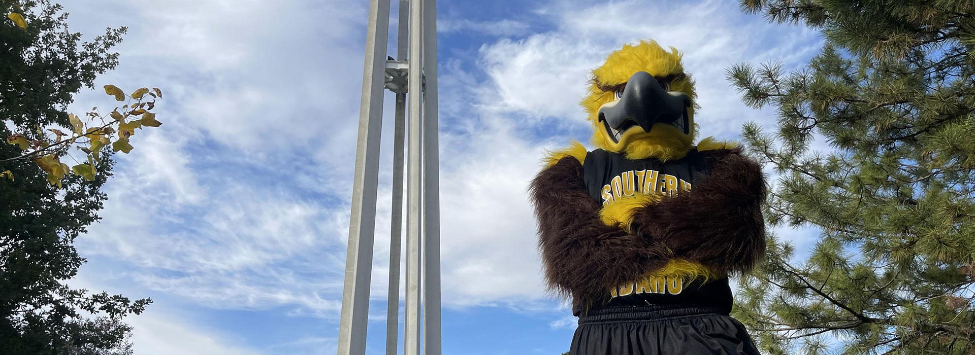 Gilbert, the CSI golden eagle mascot, faces the camera with their arms crossed.
